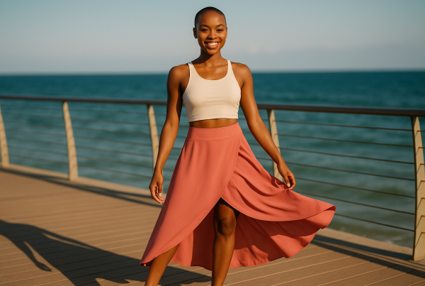 AI Model : A Black woman with a buzzcut and glowing skin stands on a sunny boardwalk overlooking the ocean, wind gently rustling her flowy high-low maxi skirt.