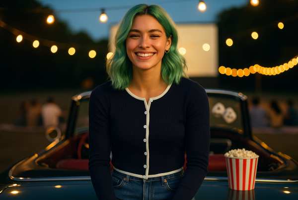 AI Model : A 22-year-old with shoulder-length, pastel mint-green hair in soft waves sits on a vintage convertible at a drive-in movie, facing straight ahead. Popcorn buckets, fuzzy dice, and string lights set a retro-cool mood as friends gather on blankets around the glowing big screen.